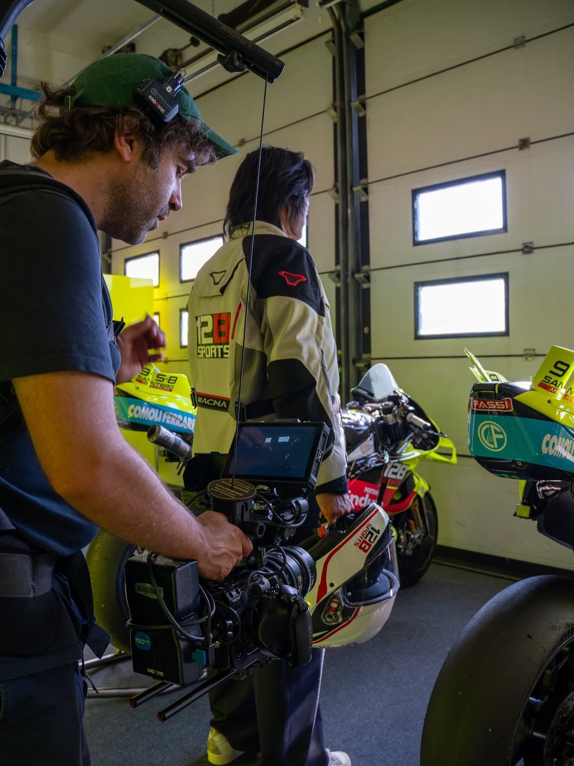 Behind-the-scenes filming inside a racing garage featuring 12B SPORTS branding, professional camera equipment and racing motorcycles.